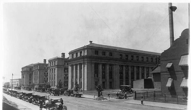 The Bureau of Engraving and Printing in Washington, a row of stone office buildings with early automobiles parked along the street